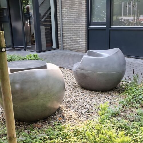 Betonnen zitelementen en tafel Stool 39 Laat uw buitenruimte opvallen met het unieke betonnen straatmeubilair van de Stool-serie – een perfecte mix van elegantie, robuustheid en praktisch ontwerp. Deze set staat in een particuliere tuin in Zevenaar.
